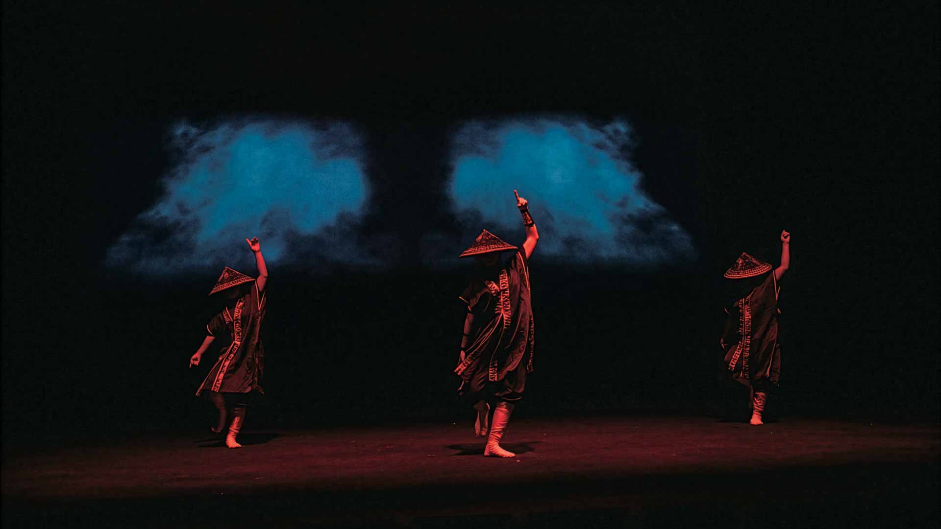 Tre dansare i traditionella okinawanska dräkter på en mörk scen